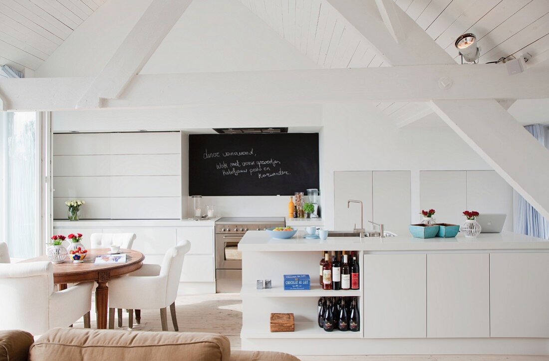 Open-plan interior with kitchen counter and dining area in renovated attic with white wood cladding