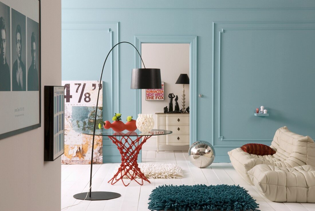Bogenlampe mit schwarzem Schirm vor Glastisch und weisses Polstersofa in Wohnzimmer mit hellblau getönten Wänden