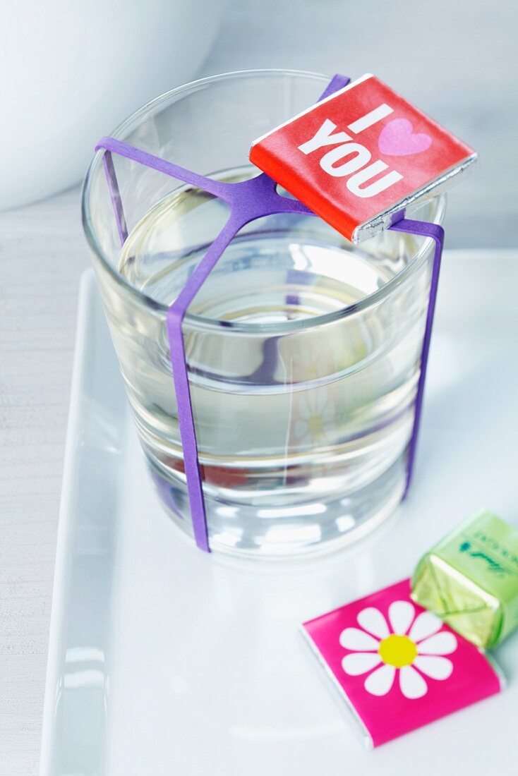 Schoko-Grüsse und ein Glas Wasser mit lila Gummiband