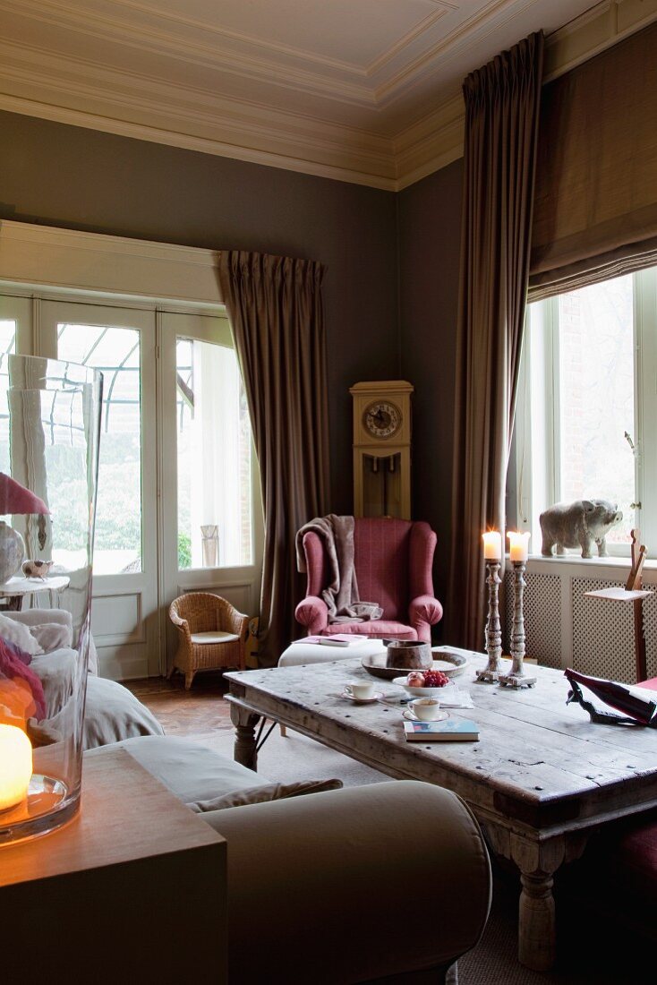 Rustikaler Couchtisch vor Sofa und Lesesessel in Zimmerecke eines traditionellen Wohnzimmers mit gerafften Vorhängen an Fenstern