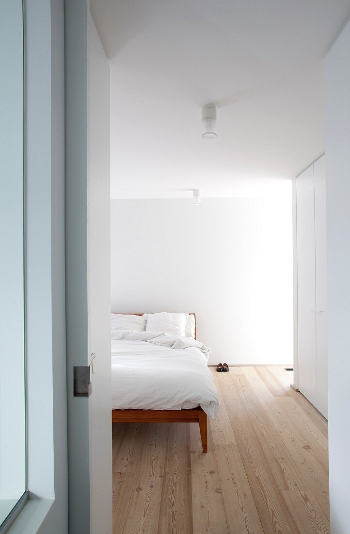View through open door into bright, modern bedroom with board floor and double bed with delicate wooden frame