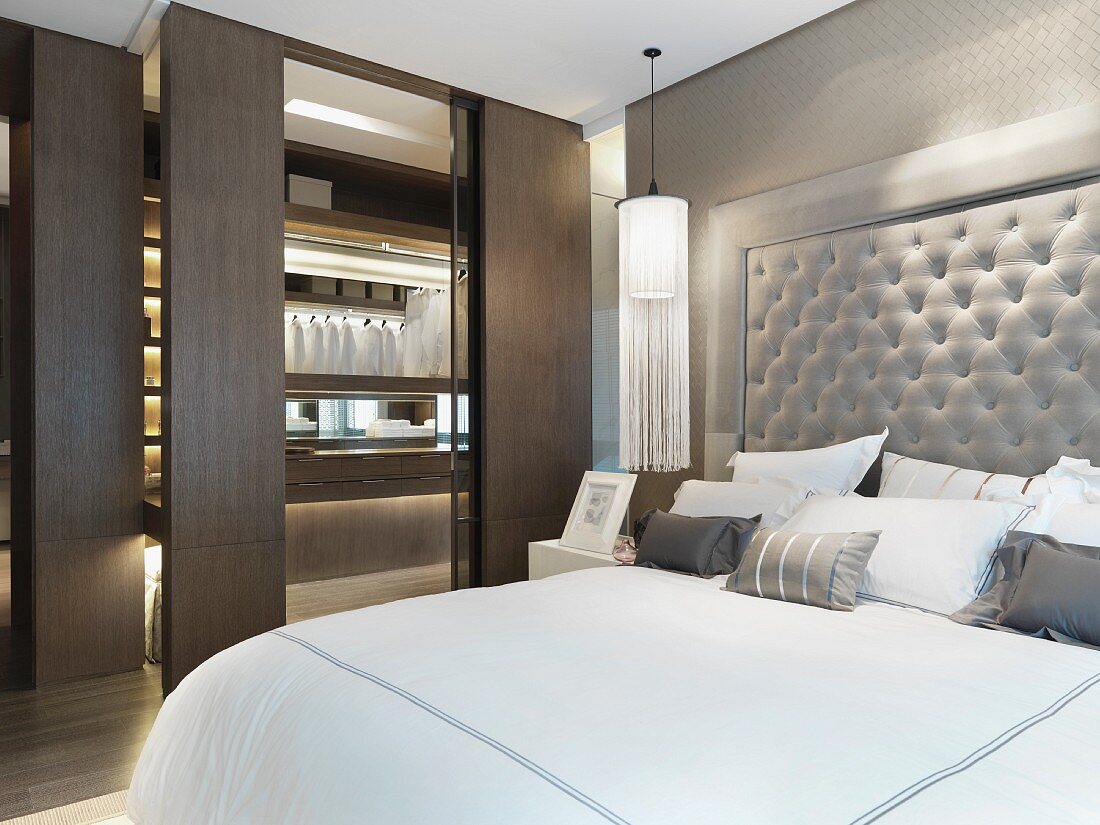 Doppelbett mit gepolstertem Kopfteil neben Ankleide mit offenen Schiebetüren im modernen Schlafzimmer