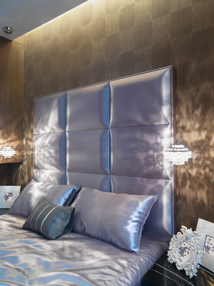 Elegantes Schlafzimmer - gepolstertes Kopfteil eines Doppelbettes und Kissen in gleichem glänzenden Stoffbezug