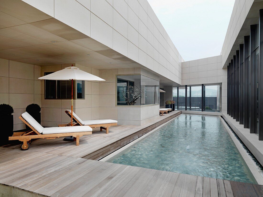 Zeitgenössische Architektur mit Liegestühlen auf Holzterrasse am Pool im Innenhof