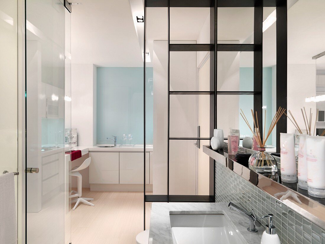 Waschbecken vor Raumteiler und offener Glastür mit Blick in weiss möblierten Raum
