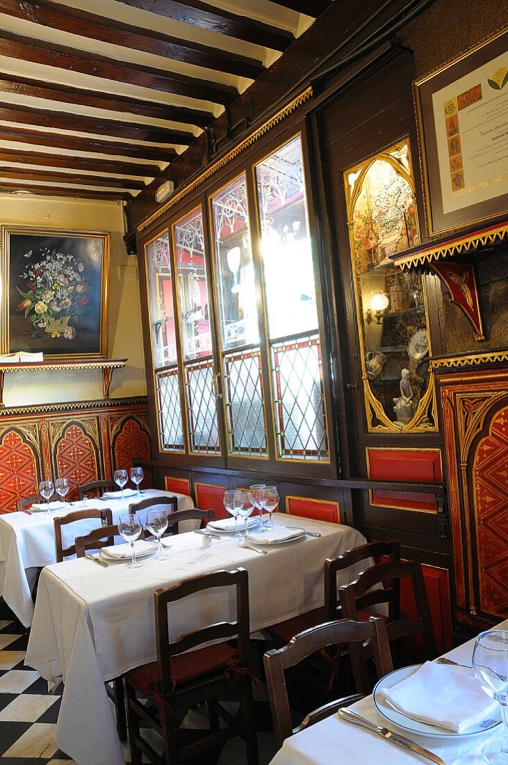 Restaurantinnenraum - Gedeckte Esstische mit weißem Tischtuch vor antiken bemalten Holzpaneelen und Holzbalkendecke