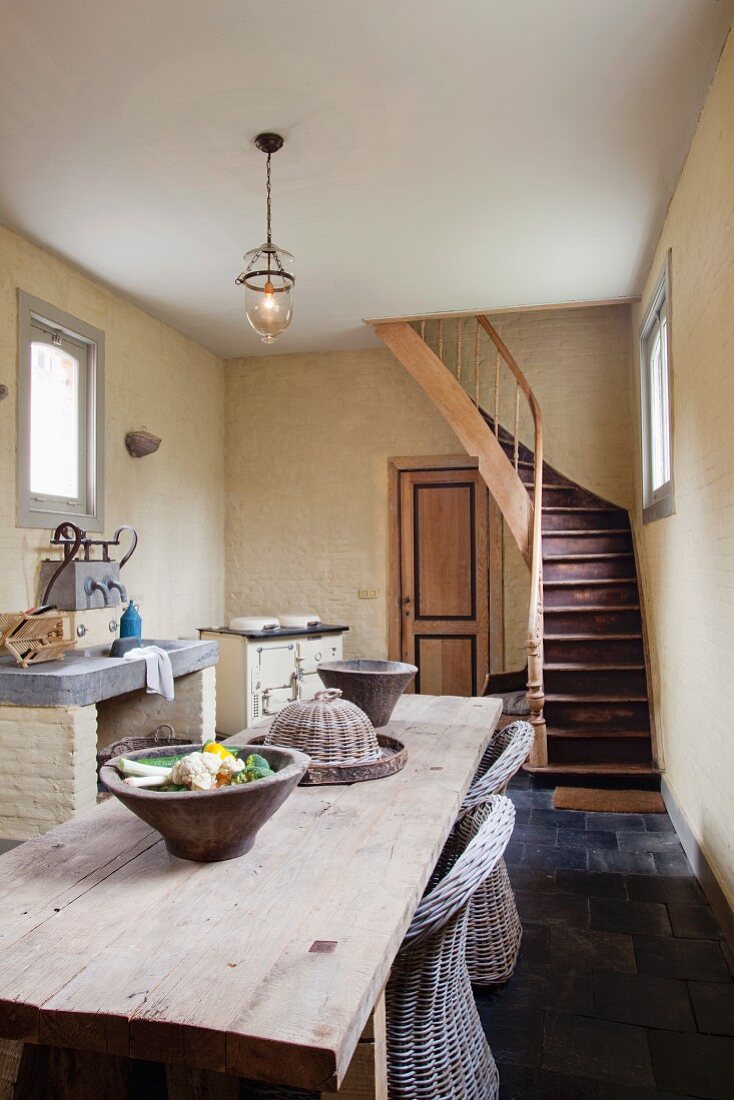 Schlichter Holztisch in offenem Esszimmer mit Küchenbereich und Treppenaufgang im Hintergrund