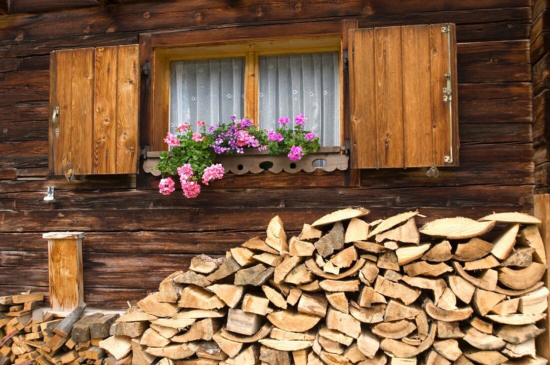 Gestapeltes Holzlager an Wand einer Blockhütte und Blumenkästen am Fenster