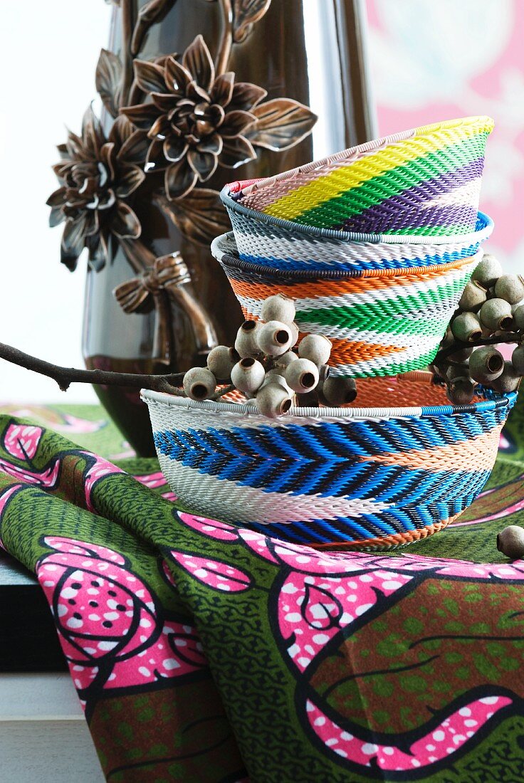 Handgeflochtene Körbchen aus buntem Draht vor einer Vase mit Blumenrelief auf afrikanischem Stoff
