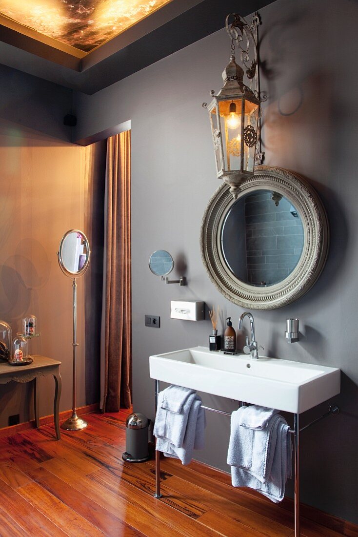 Designer bathroom with grey walls, trough-like sink with metal frame and round vintage mirror on wall