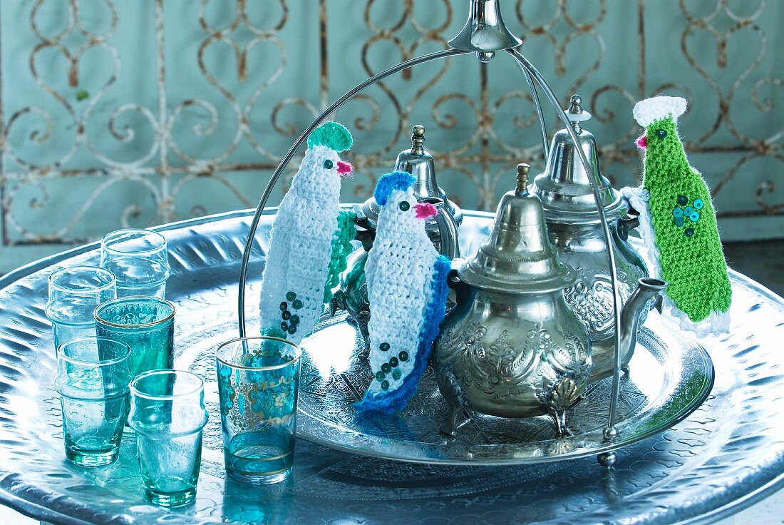 Runde Metallschale mit orientalischen Teekannen und Finger Wärmeschutz am Griff auf Tablett neben farbigen Teegläsern
