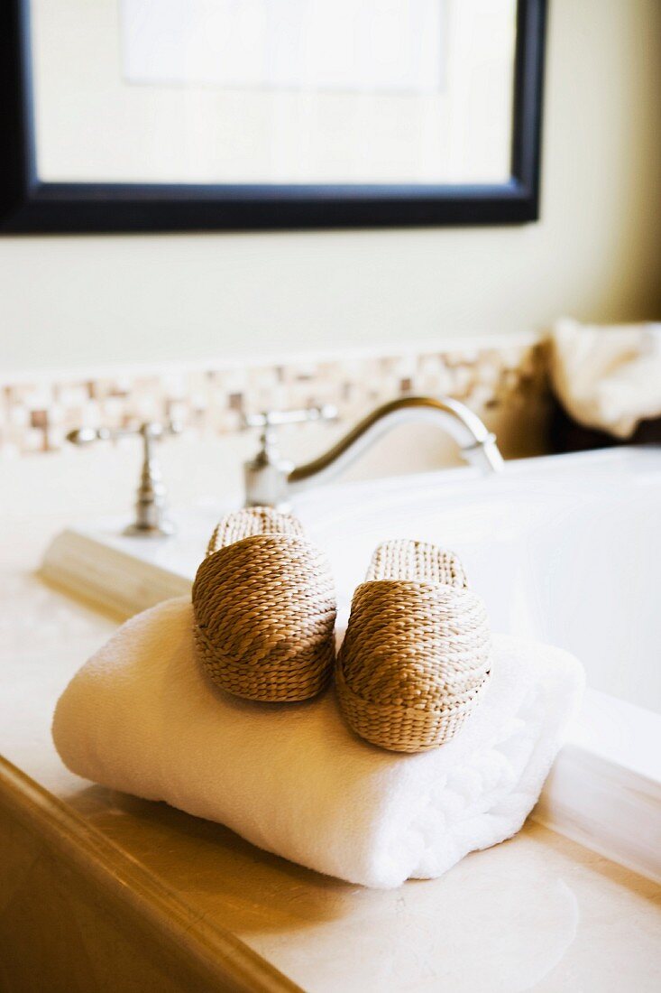 Hausschuhe aus Bast auf Handtuch neben Badewanne