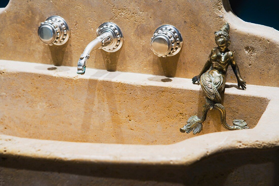 Old stone sink with wall-mounted taps and brass figurine of a woman
