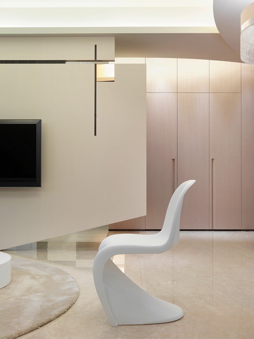 Klassiker Schalenstuhl aus weißem Kunststoff und zeitgenössischer Raumteiler mit aufgehängtem Fernseher