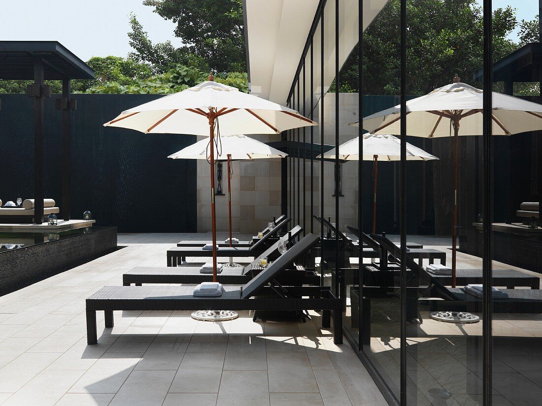 Zeitgenössische Outdoormöbel mit Sonnenschirm auf gefliester Terrasse vor Glasfassade eines Wohnhauses