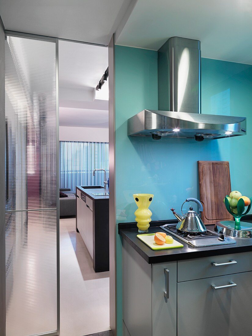 Küchenzeile mit Dunstabzug aus Edelstahl neben halb offener Glastür und Blick in Nebenraum
