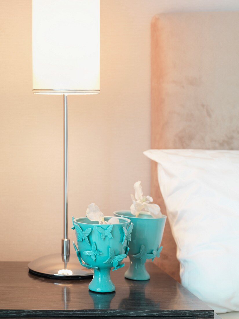Decorative, turquoise goblets and table lamps on bedside table