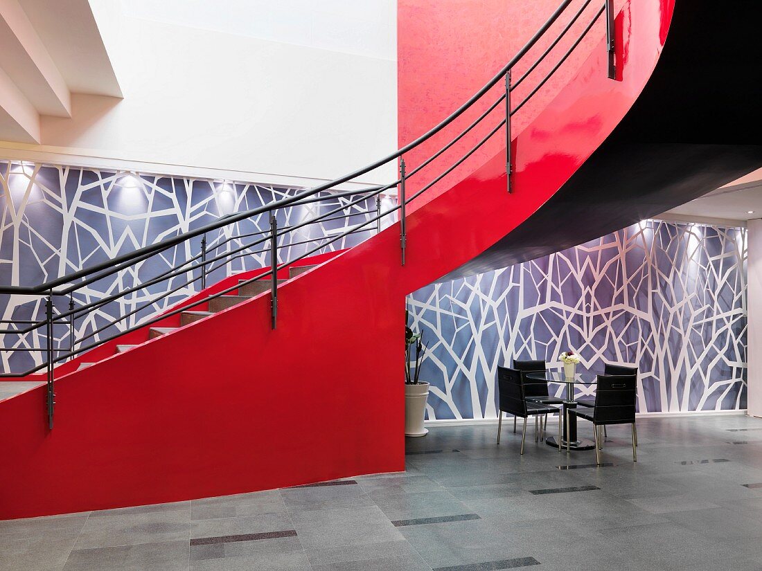 Geschwungene Treppe mit roter Wangenwand vor gestalteter Wand in grosszügigem Foyer
