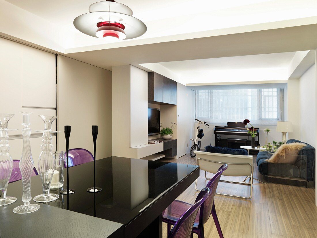Esstisch mit spiegelnder, schwarzer Oberfläche und Deckenlampe im Fiftiesstil in offenem Wohnraum