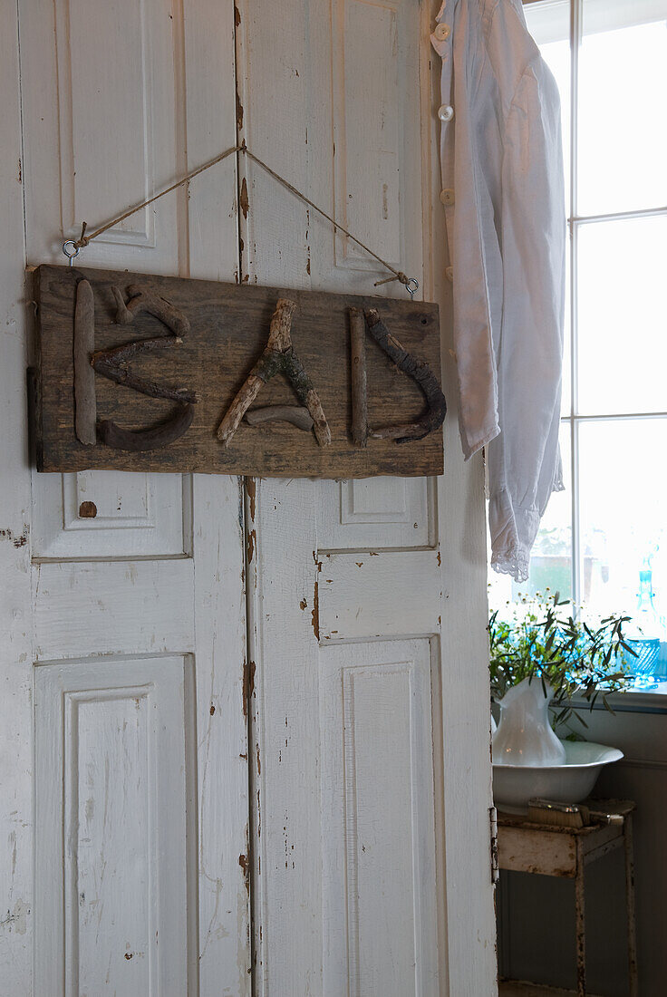 Sign made of branches with the inscription "BAD" on a white wooden door