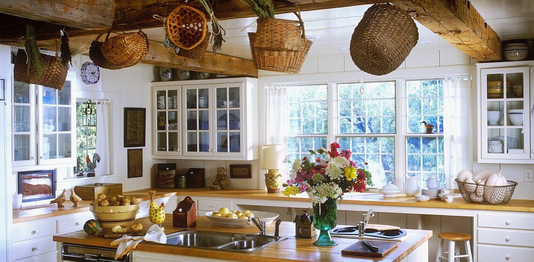 Bright, country-house kitchen with island and baskets hanging from beamed ceiling