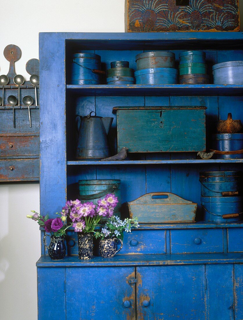 Blue, vintage-style kitchen dresser holding collection of blue kitchen utensils and three posies of summer flowers