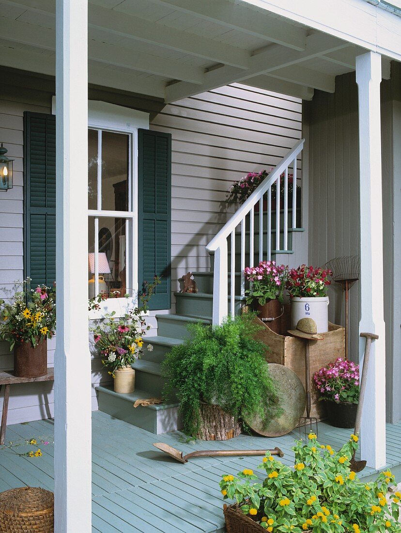 Foot of staircase with cheerful planters outside wooden house with roofed veranda