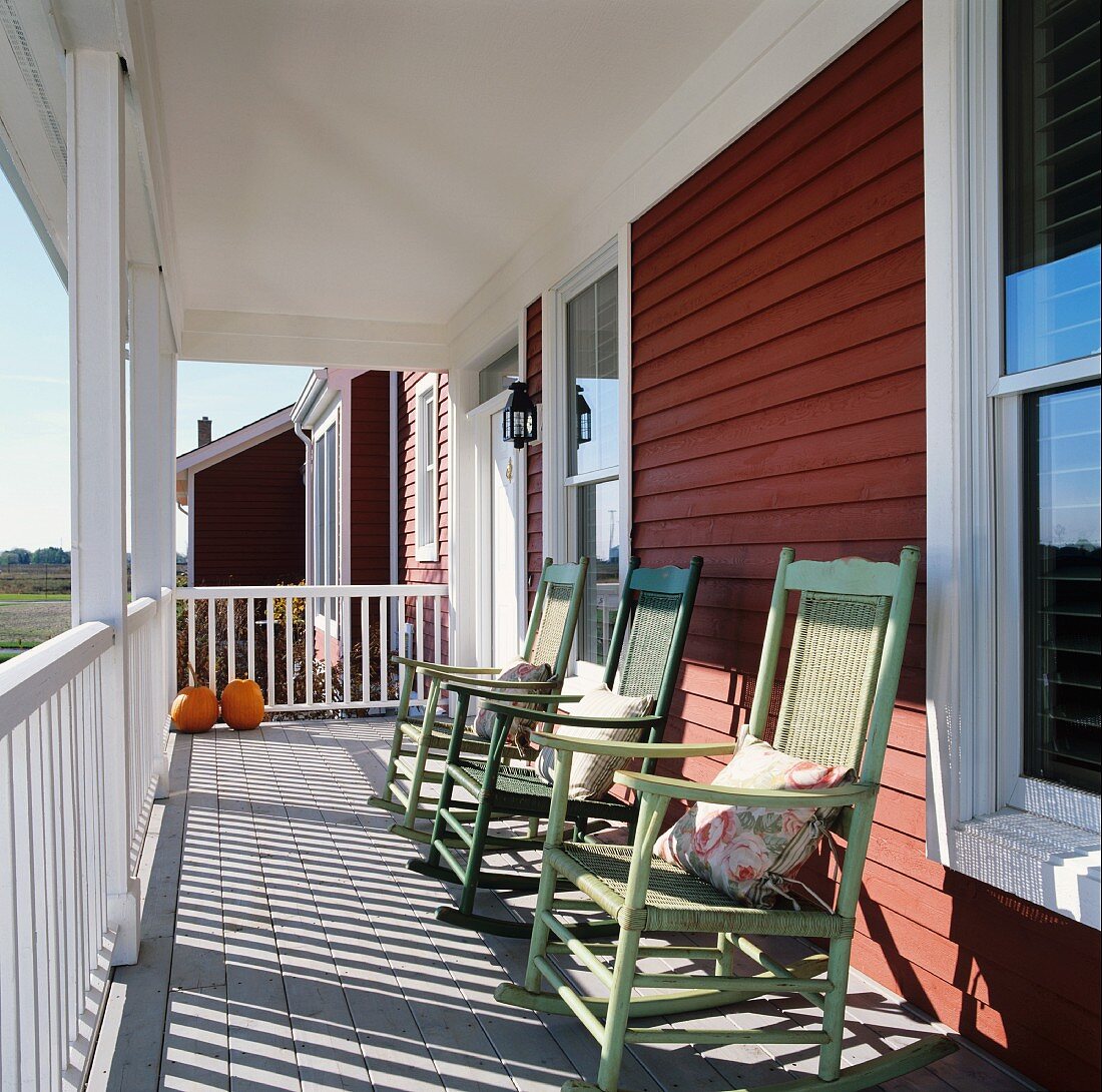 Row of rocking chairs on sunny, roofed veranda of wooden house