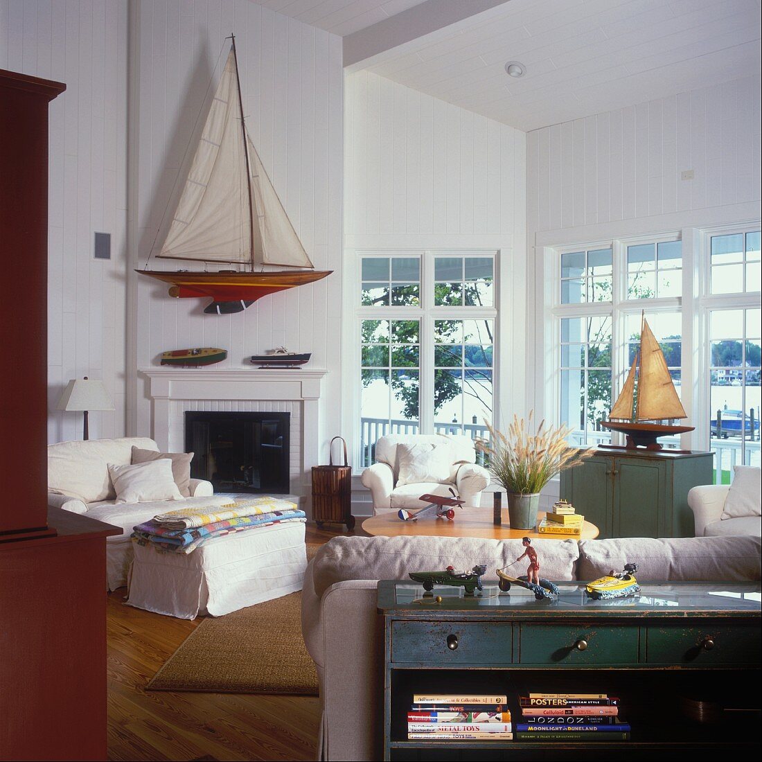 Wohnzimmer mit breiter Fensterfront und einem großen Modell-Segelboot über dem offenen Kamin