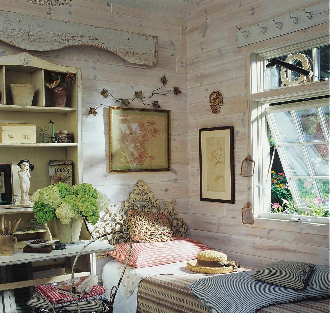 Ländlicher Raum mit Holzwänden, einem Einzelbett mit kunstvollem Kopfende und einem weissen Hortensienstrauss