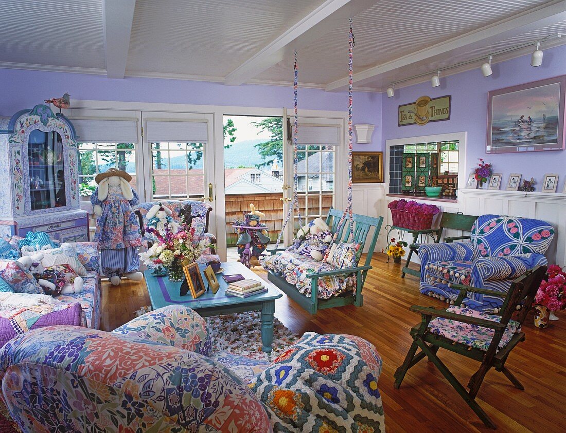 Interior with open balcony door, furniture upholstered in various pastel patterns and serving hatch to kitchen