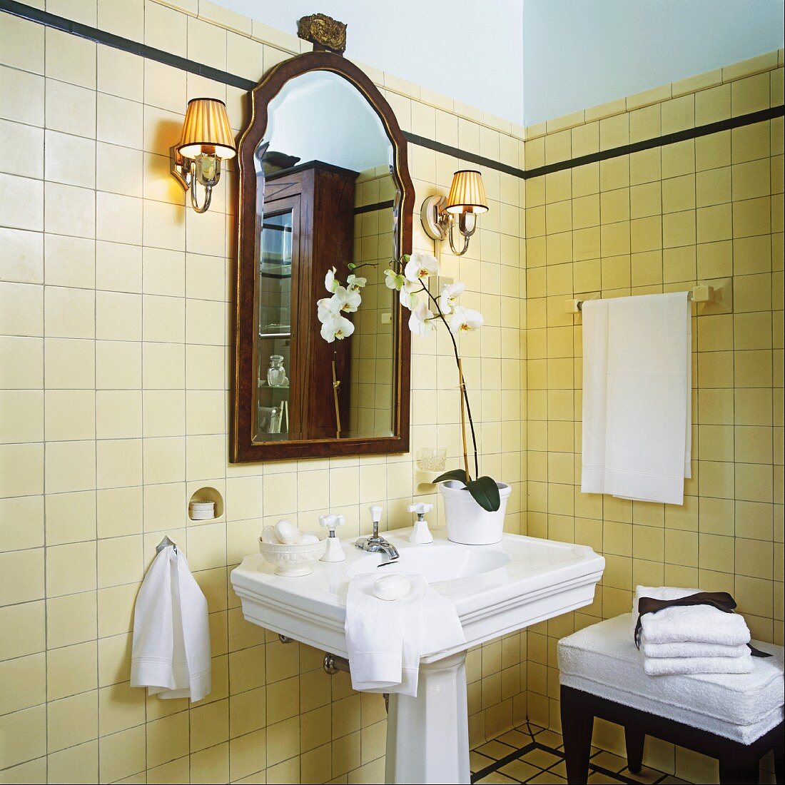 Antikes Badezimmer mit Standwaschbecken, mit cremefarbenen Wand- und Bodenfliesen und mit einer blühenden Orchidee