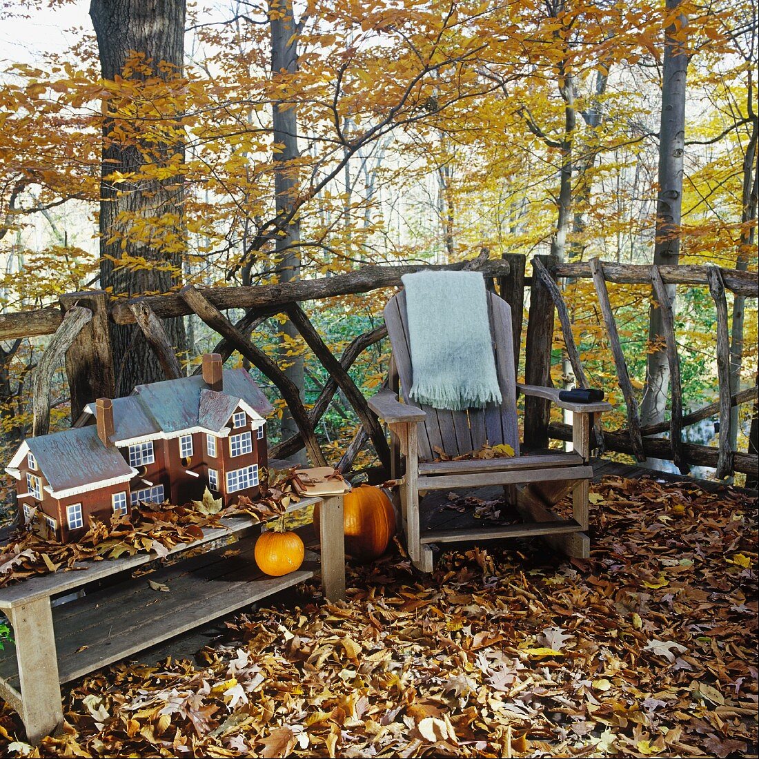 Herbstliche Terrasse mit rustikalem Lehnstuhl und einem Laubteppich; daneben ein Hausmodell auf einem Holztisch