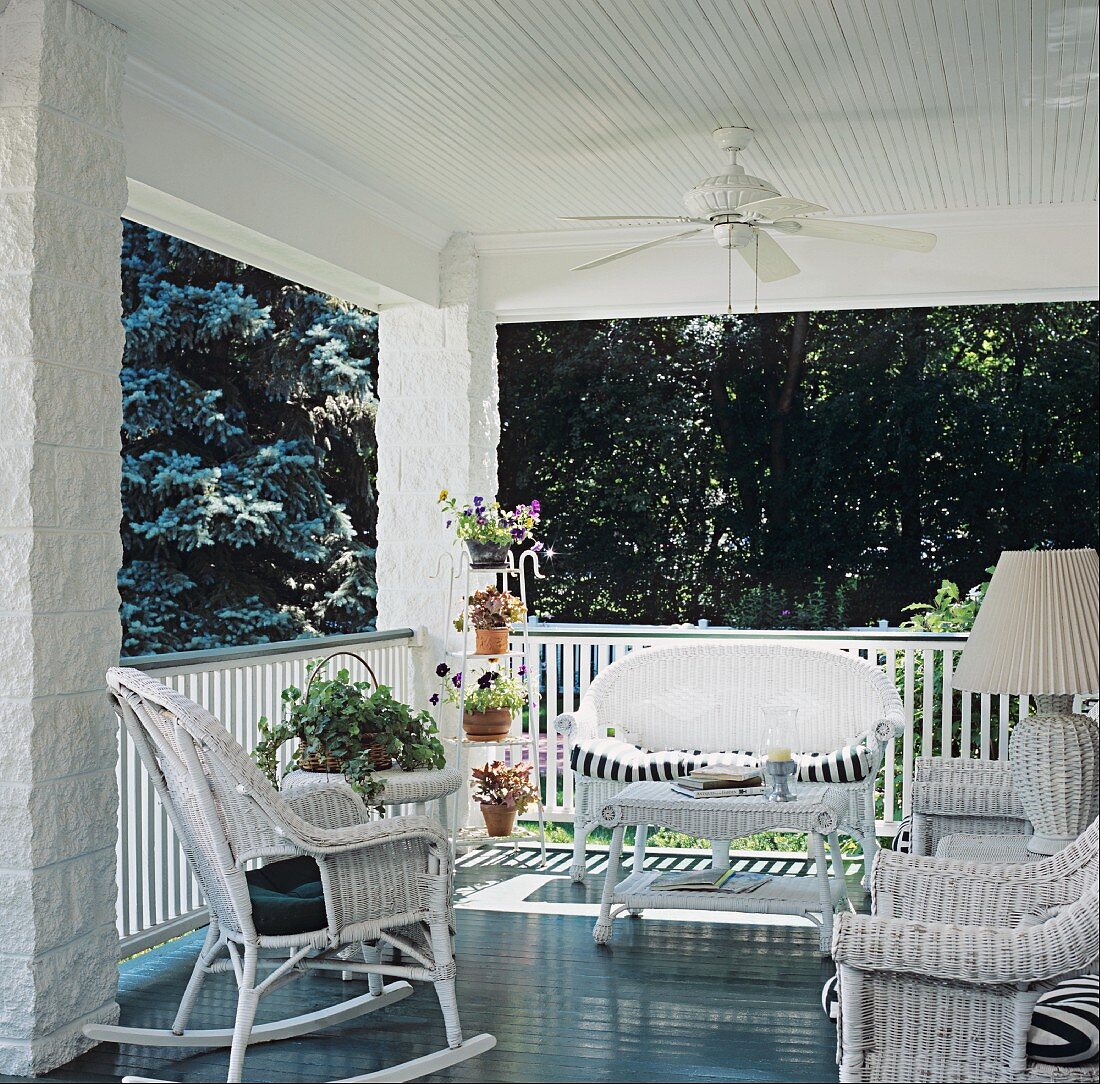 Roofed veranda with ceiling fan, white wicker furniture and table lamp with wicker base