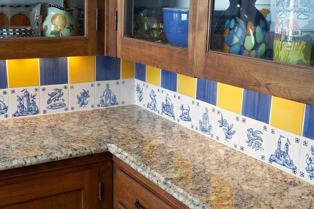 Detail of kitchen corner with granite worksurface and decorative wall tiles in blue and yellow above row of original, unique tiles with blue patterns