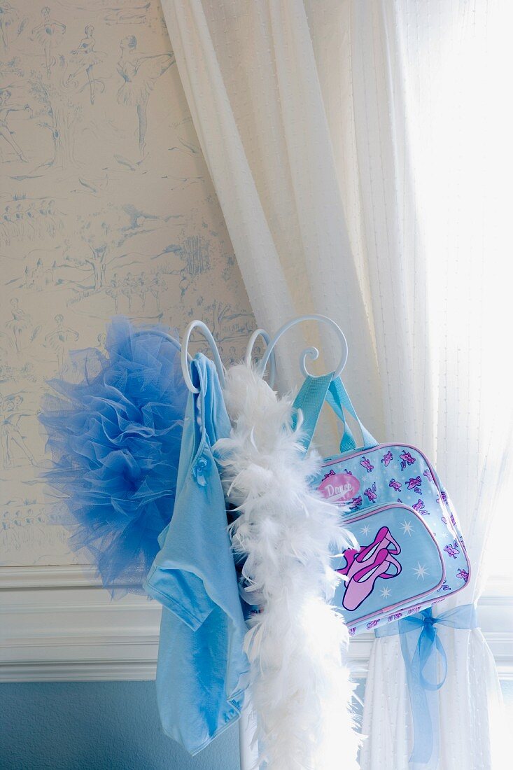 Garderobe mit Federboa und Handtasche vor Fenster mit weißem Vorhang