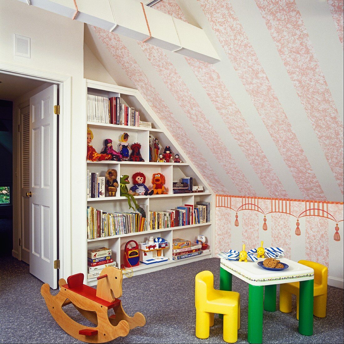 Corner of child's attic bedroom with books and toys on shelving, children's furniture and wooden rocking horse