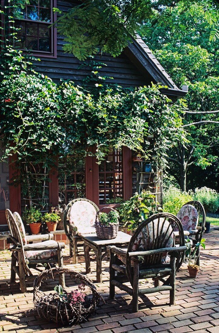 Paved terrace with rustic wooden furniture in front of wooden house with vine-covered pergola
