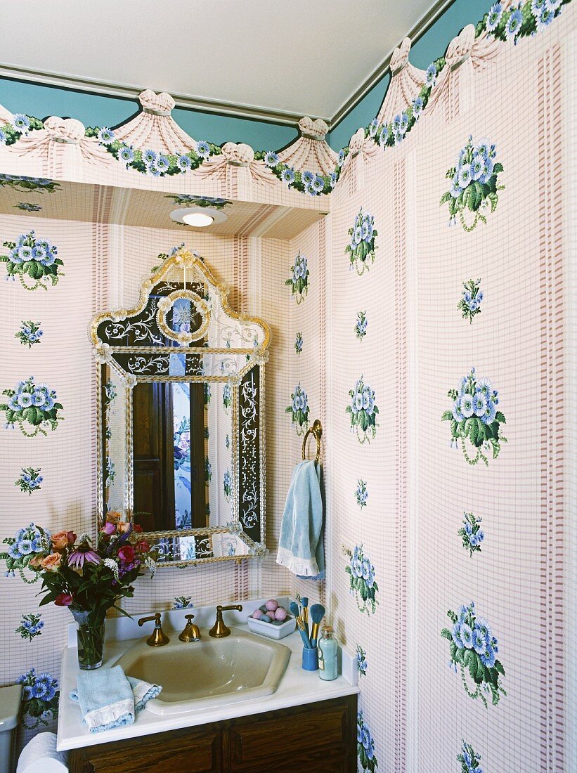 Nostalgische Ecke in einem Badezimmer mit Blumenmuster, einem Holzwaschtisch, einem Spiegel im venezianischen Stil und Schminkutensilien