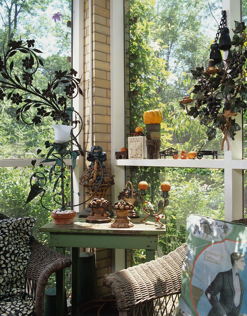 Ecke einer verglasten Veranda im Grünen mit Vintage-Tisch, Korbstühlen und Terrakottadeko