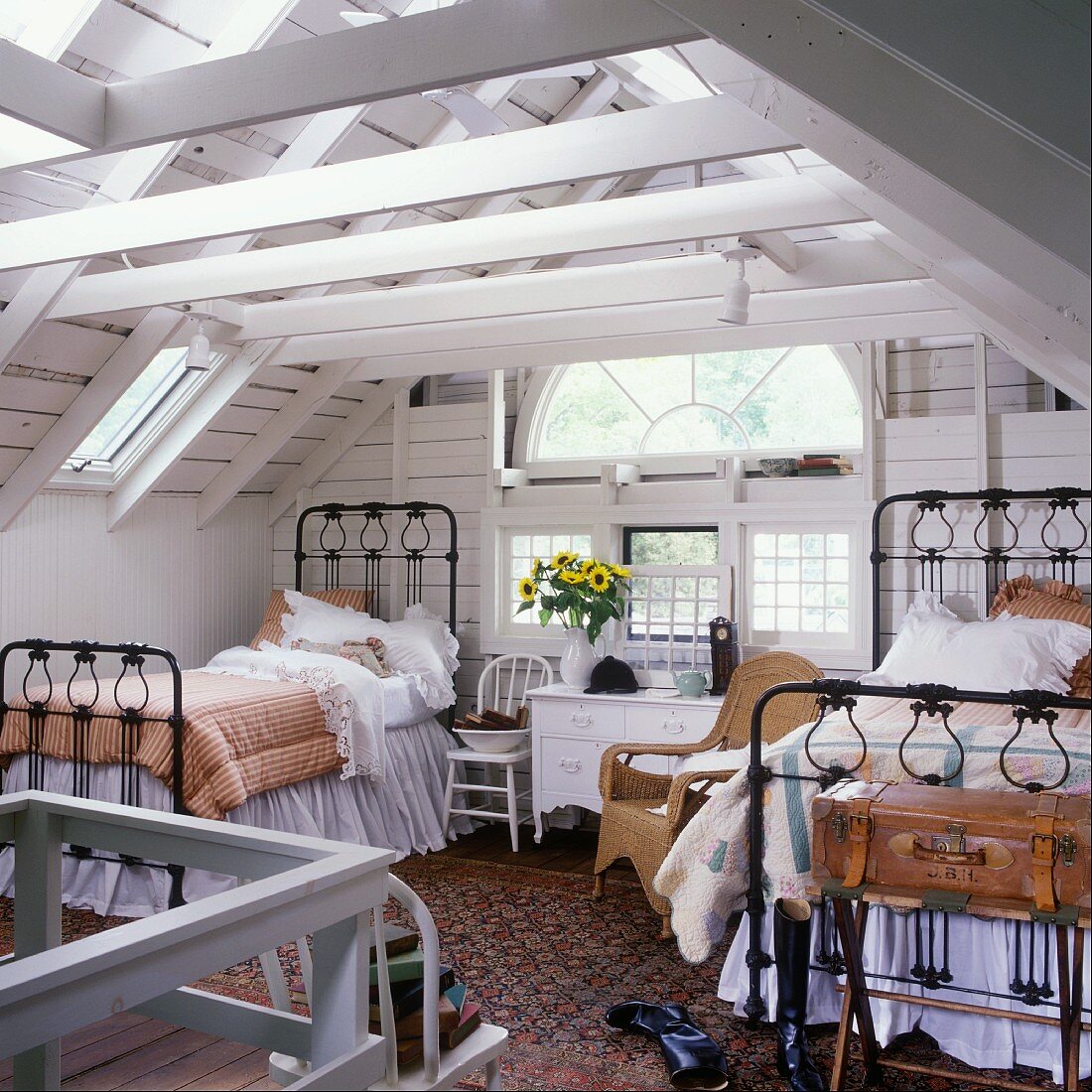 Zwei schwarze Eisenbetten und ein halbrundes Fenster in weißem Schlafzimmer mit Holzwänden unter dem Dachstuhl