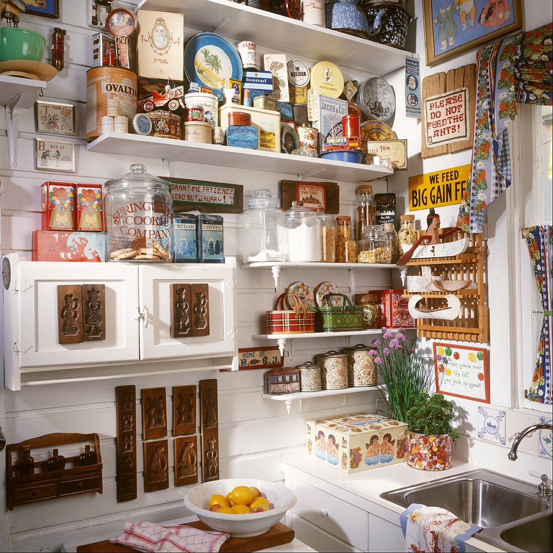 Regalwand in der Küche mit einer großen Dosen- und Raritätensammlung; ein kleines Küchenschränkchen ist mit alten Holzmodeln dekoriert
