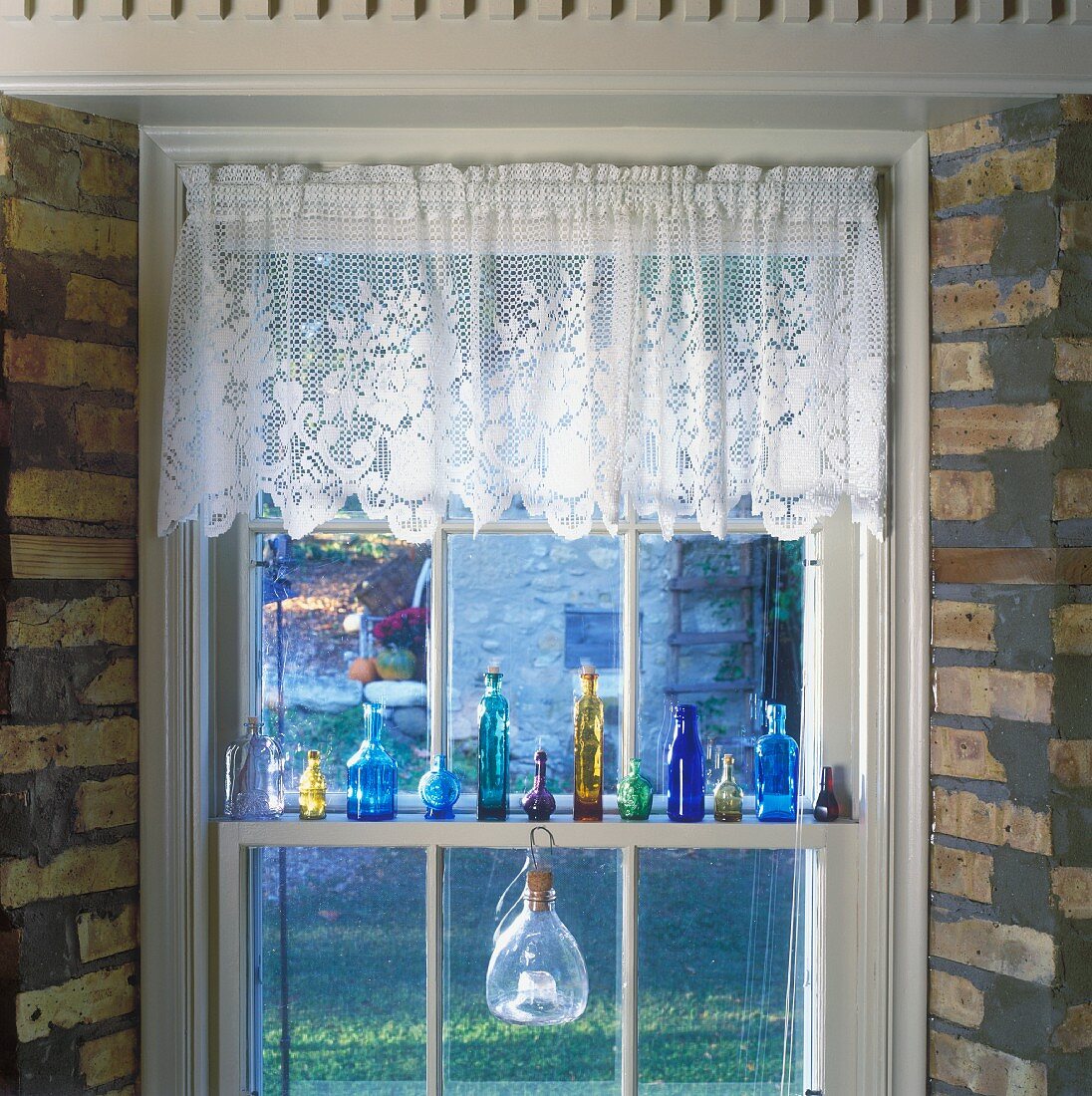 Decorated lattice window with lace curtain and collection of small glass bottles