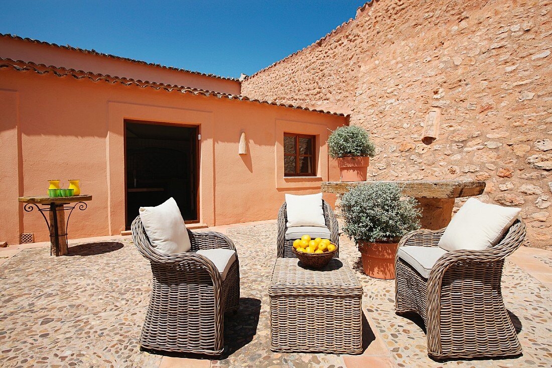 Terrassenmöbel aus Rattan im Innenhof mit Natursteinbelag vor spanischem Wohnhaus