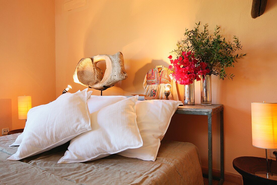 Kissen auf Bett vor Wandtisch und Nachttische mit Leuchten vor orange getönter Wand