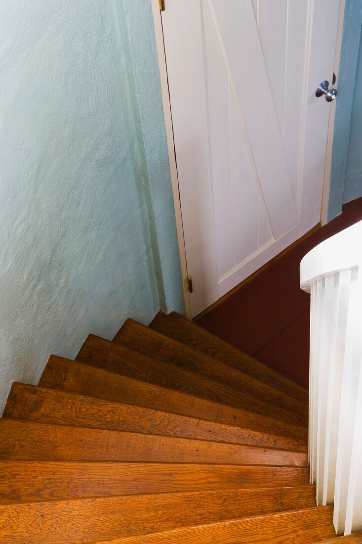 Blick von gewendelter Holztreppe nach unten auf weiße Brettertür und pastellblaue Wand