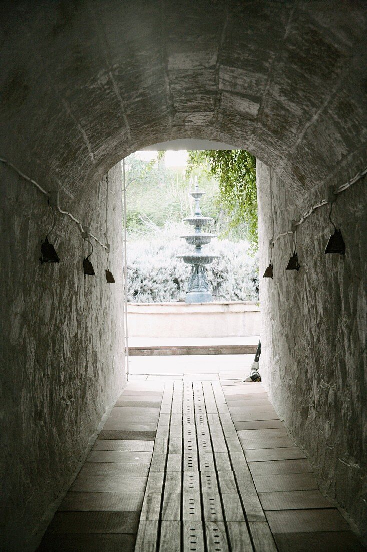 Blick auf hohen Schalenbrunnen am Ende eines holzbelegten Tunnelgangs