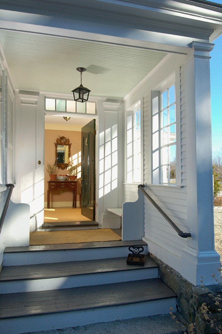 Blick über Zugangstreppen und die geöffnete Haustür in den sonnigen Vorraum einer traditionellen Landhausvilla