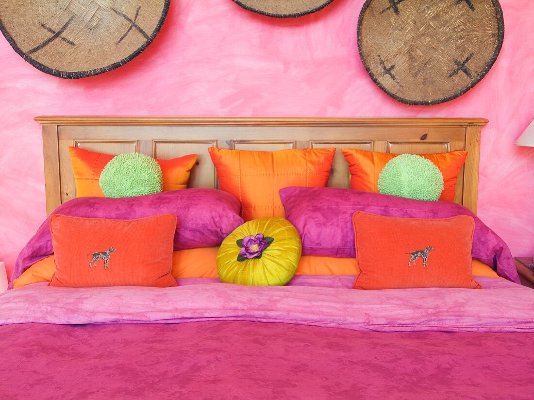 Farbrausch auf dem Doppelbett mit orange- und pinkfarbenen Kissen vor rosa marmorierter Wand