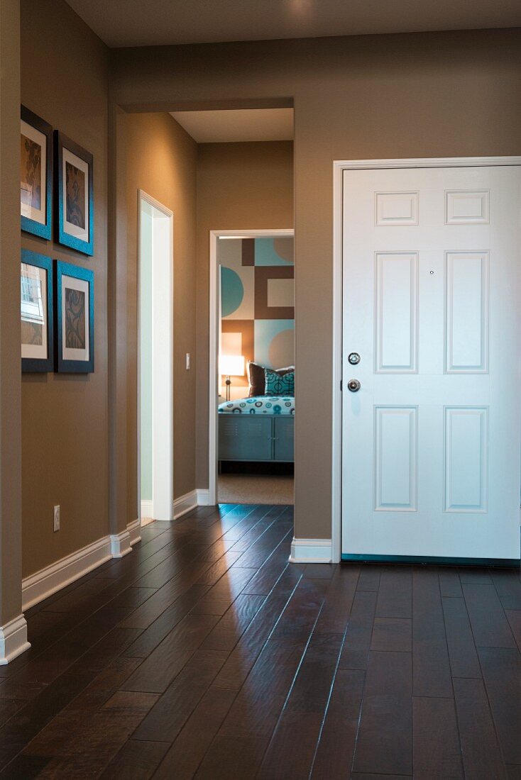 Eingangsdiele mit dunklem Holzparkett zu elegant braunbeiger Wand und offene Tür zum Schlafzimmer